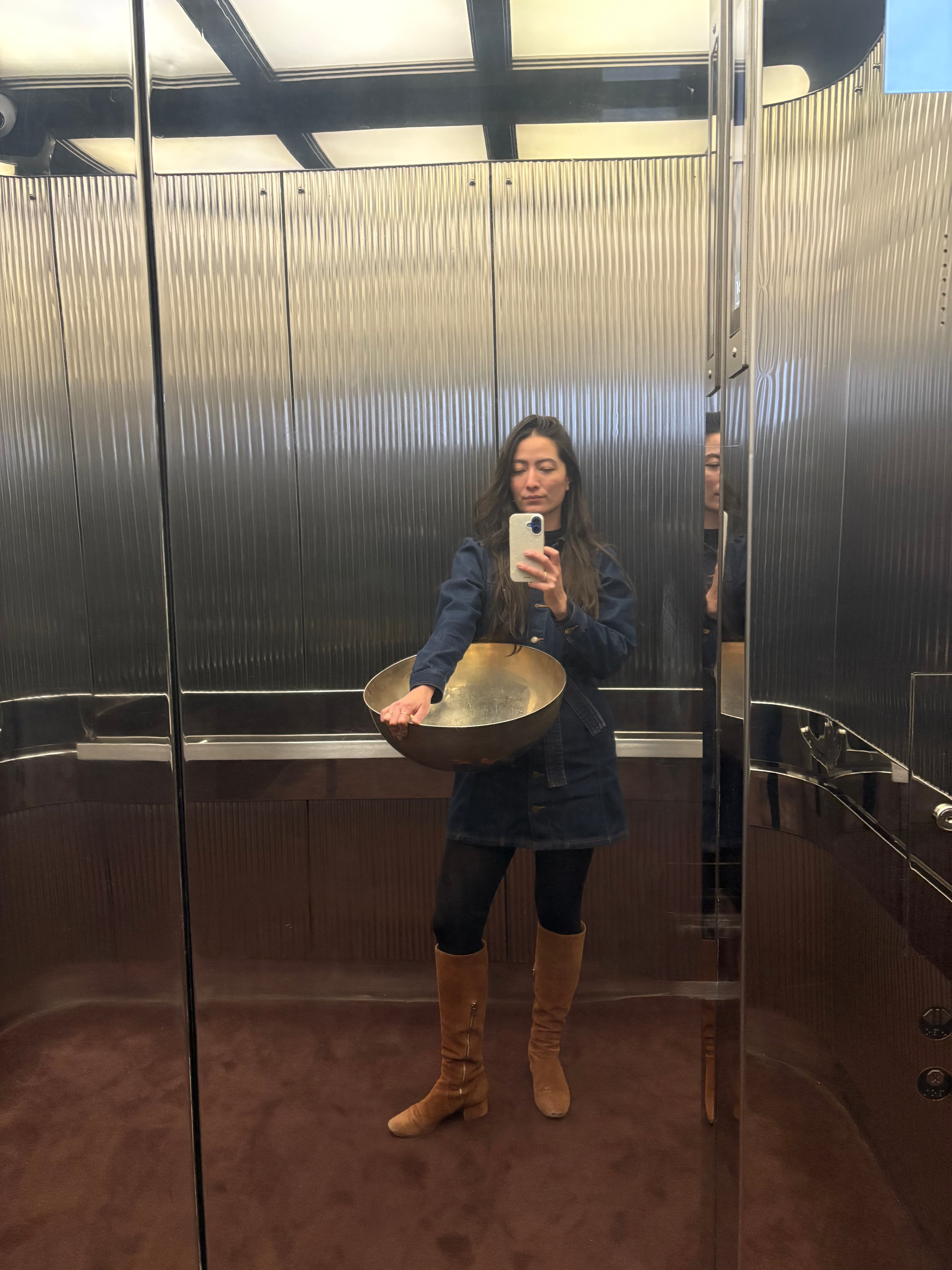 Natasha David holding a brass bowl in a mirrored elevator