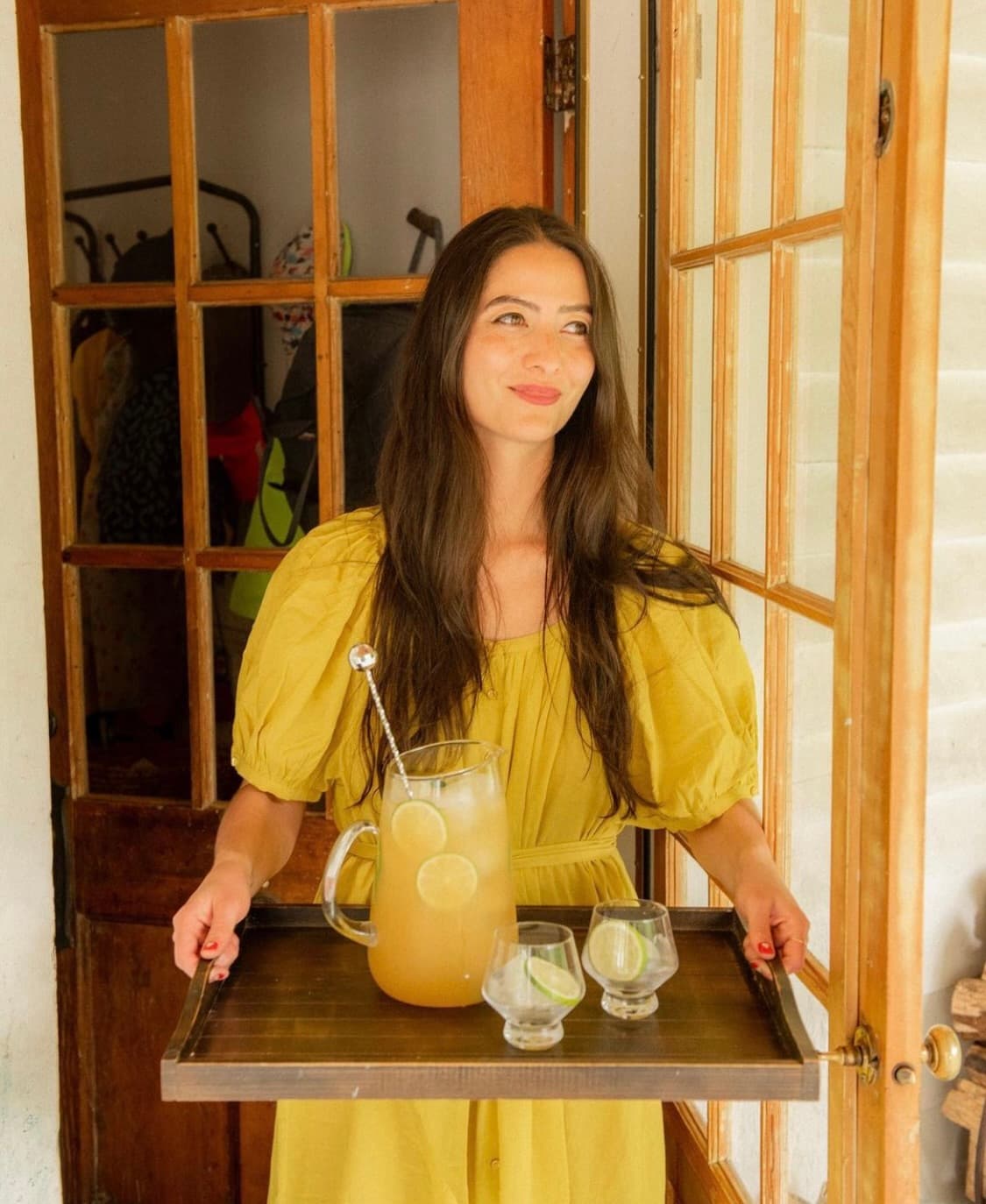 Natasha David in a yellow dress carrying a tray of drinks