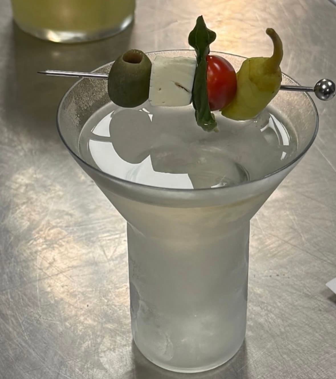 Clear martini with an olive, cheese, basil, tomato, and pepper garnish