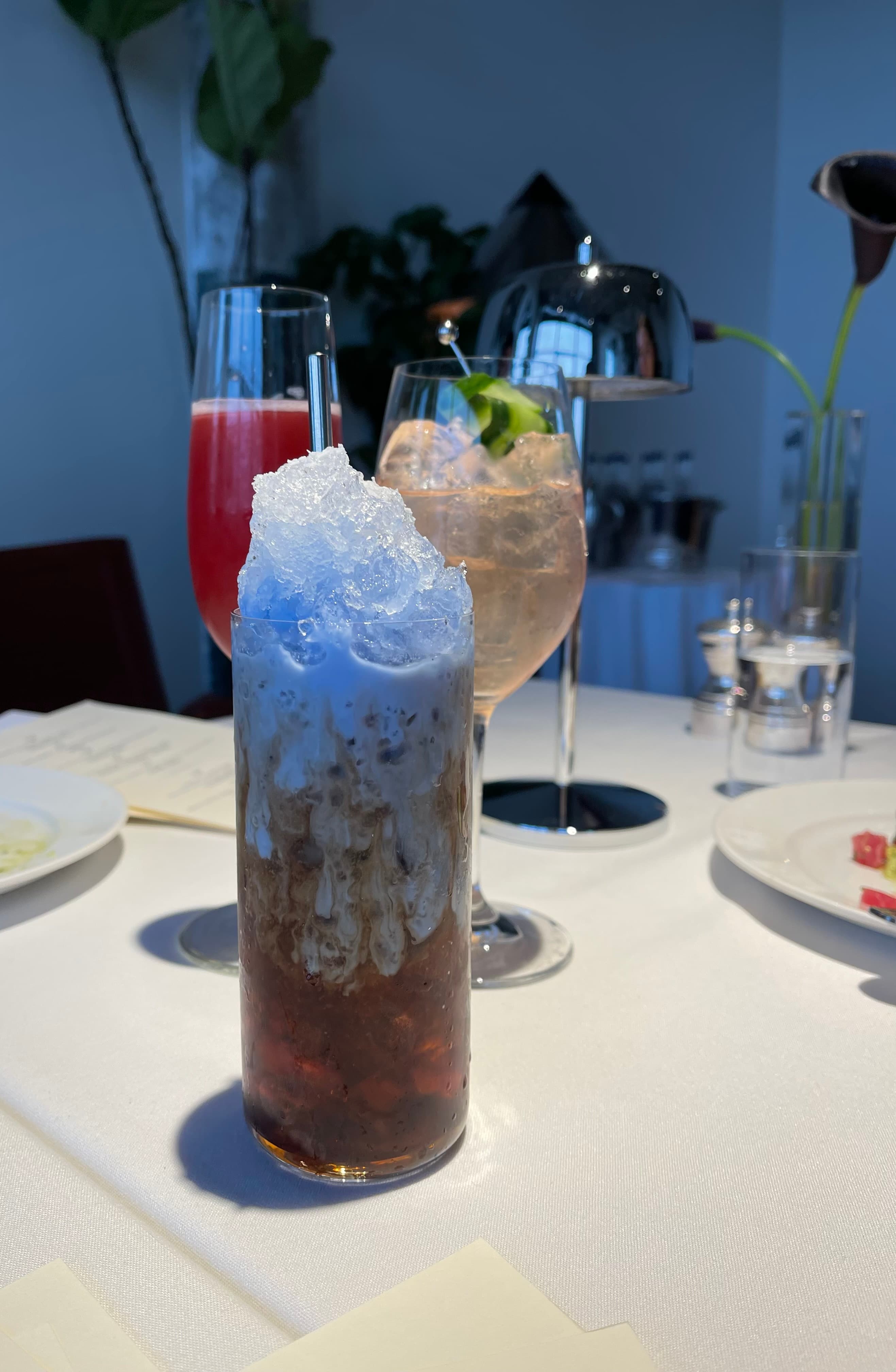 Blue shaved-ice drink with two colorful cocktails behind it