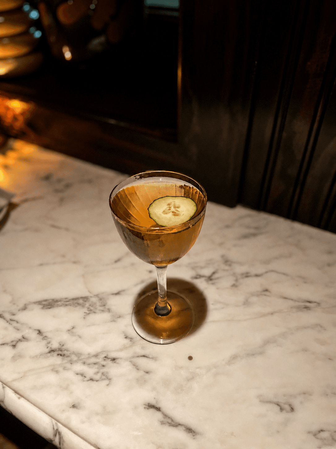 Amber cocktail garnished with cucumber in a coupe glass