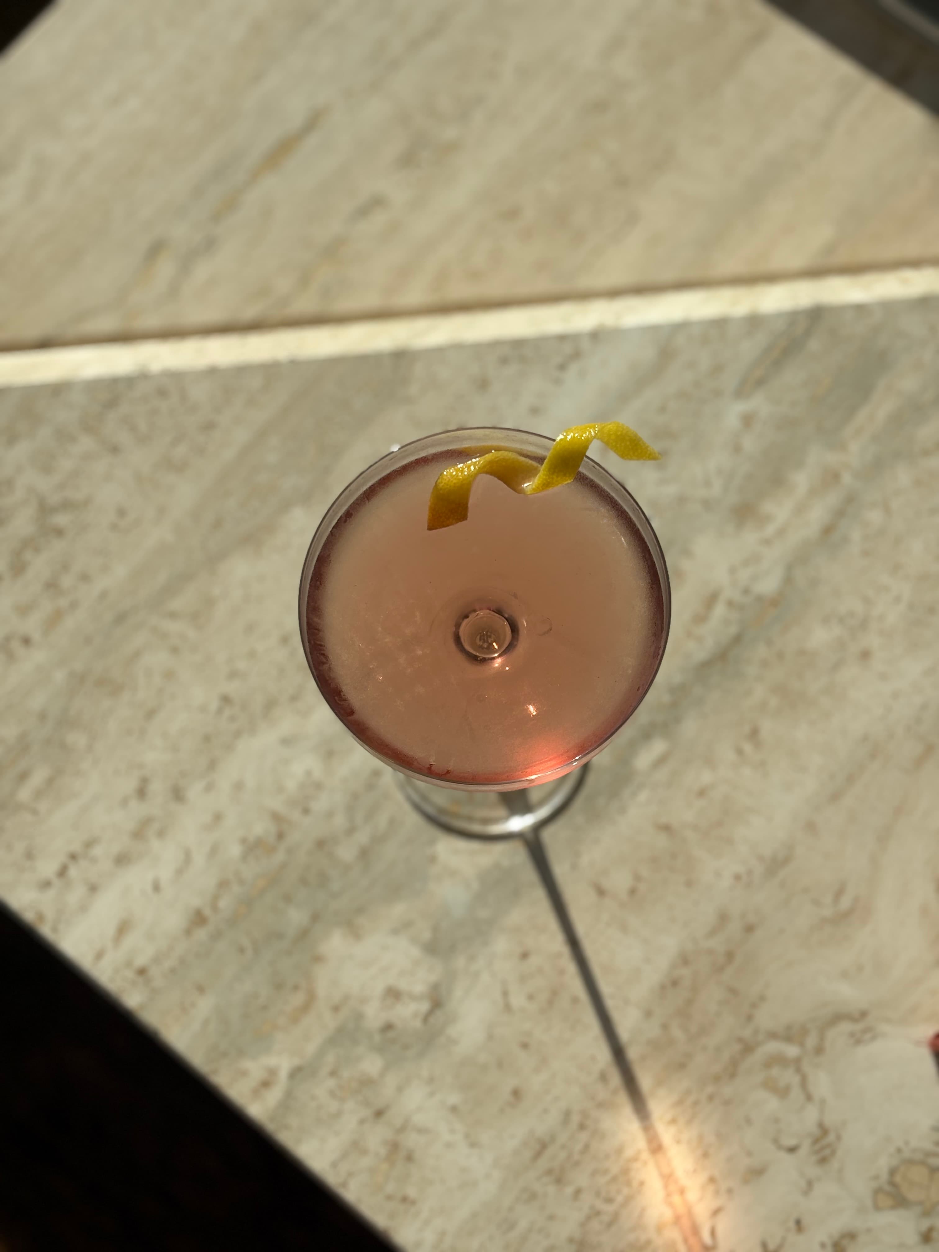 Pale pink coupe cocktail garnished with a lemon twist