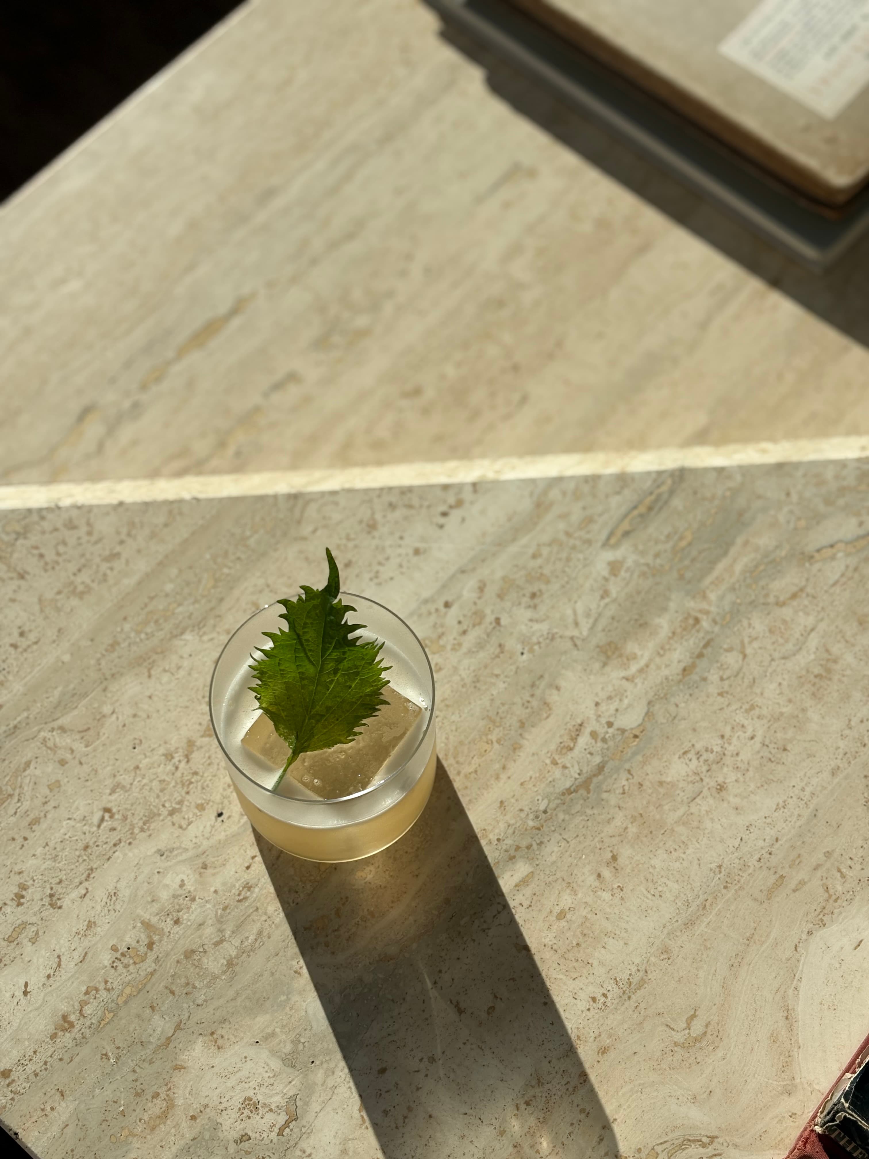 Pale cocktail over a large ice cube garnished with a shiso leaf