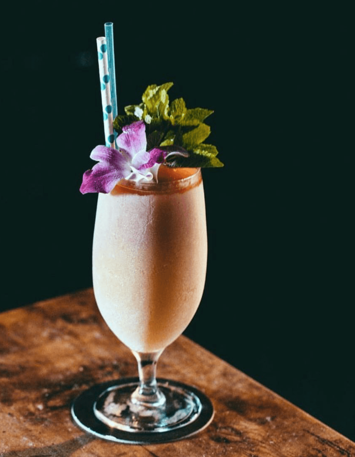 Frozen cocktail garnished with an orchid and mint on a wooden bar