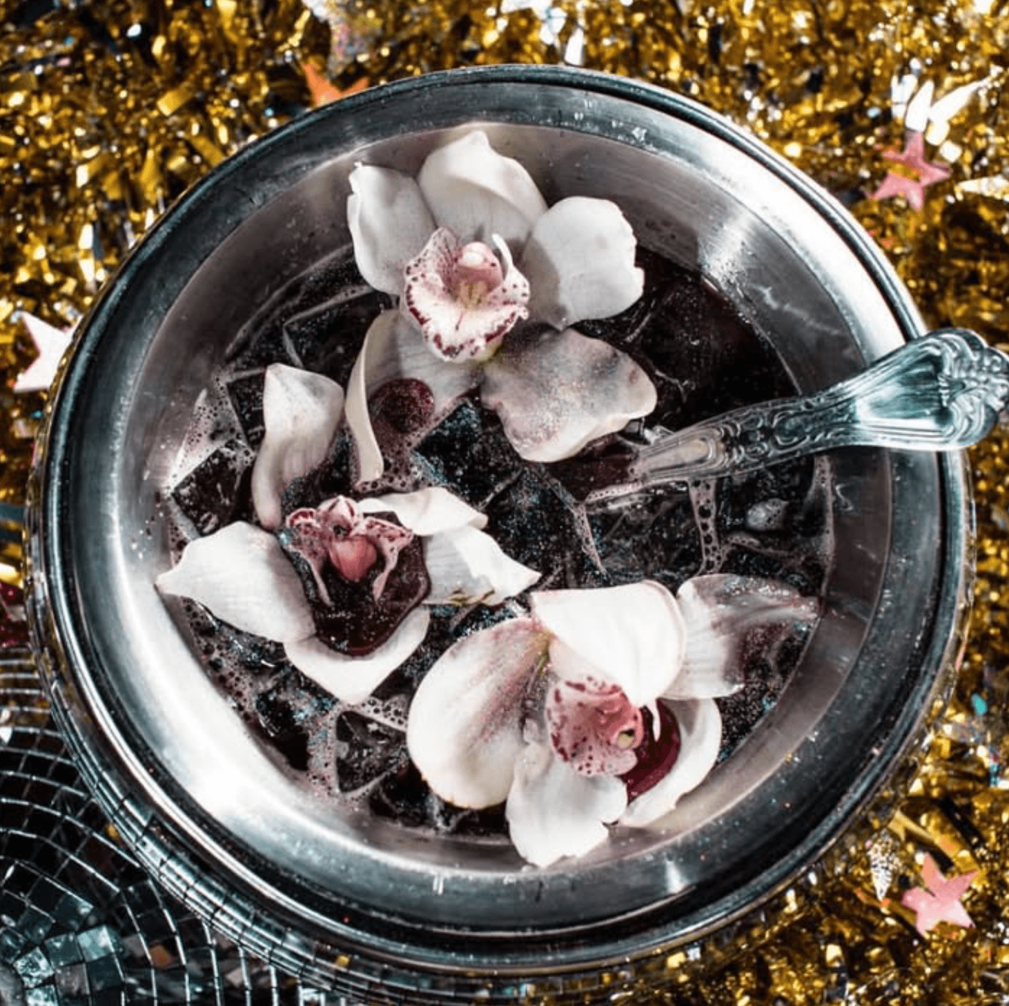 Overhead view of a dark floral punch with orchids in a silver bowl