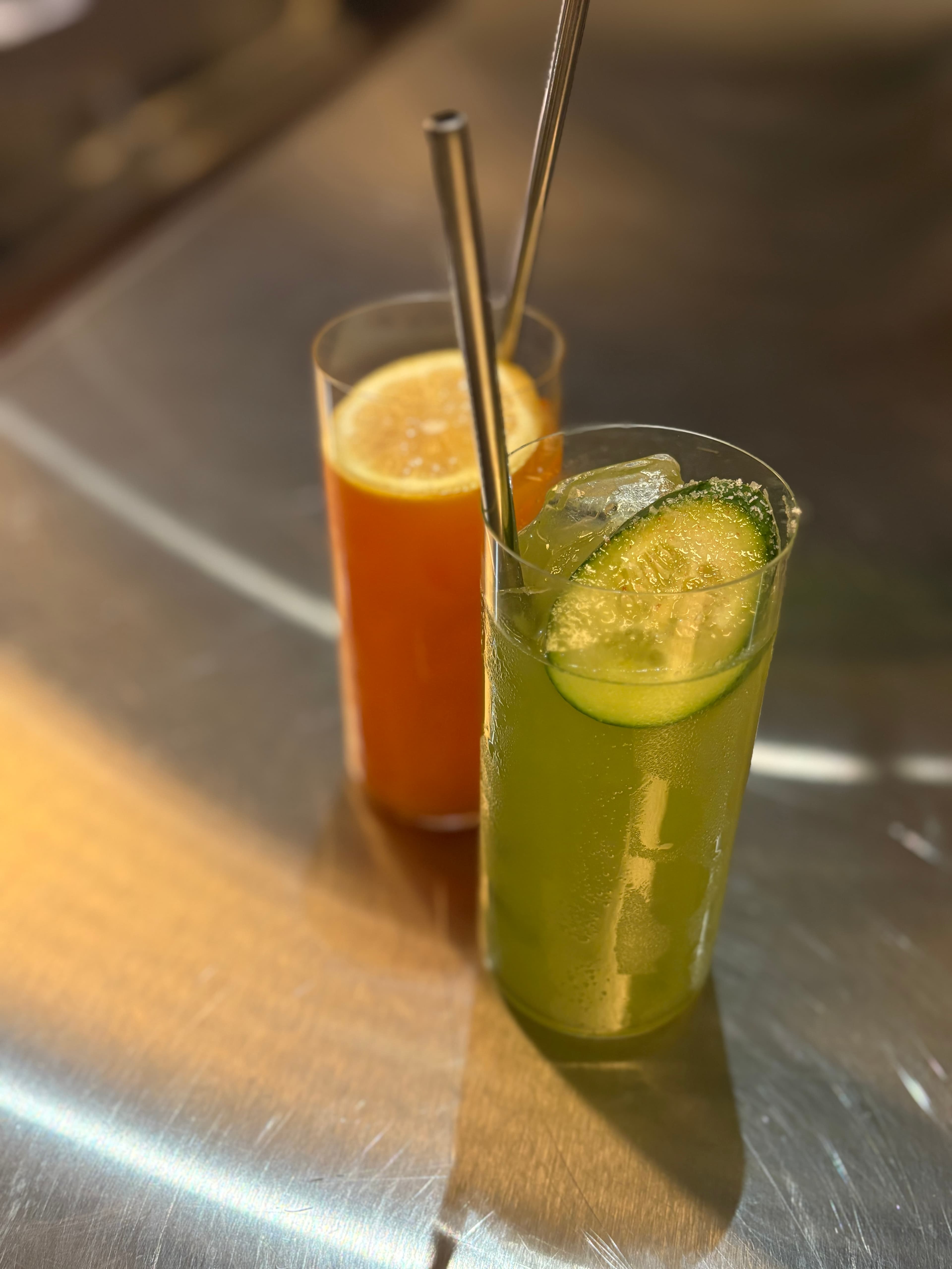 Green cucumber highball and amber citrus highball on a metal bar