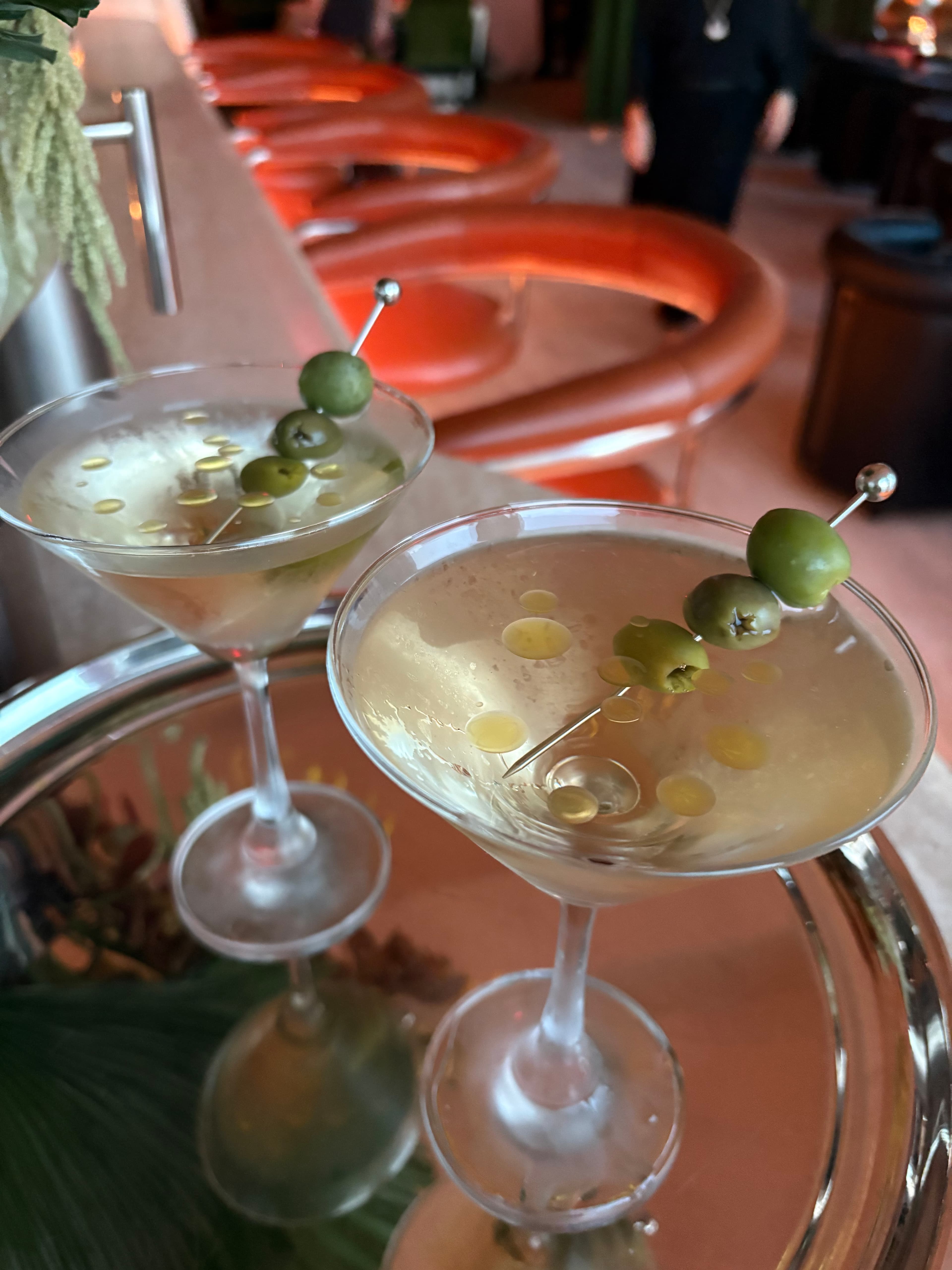 Two martinis garnished with green olives on a silver tray