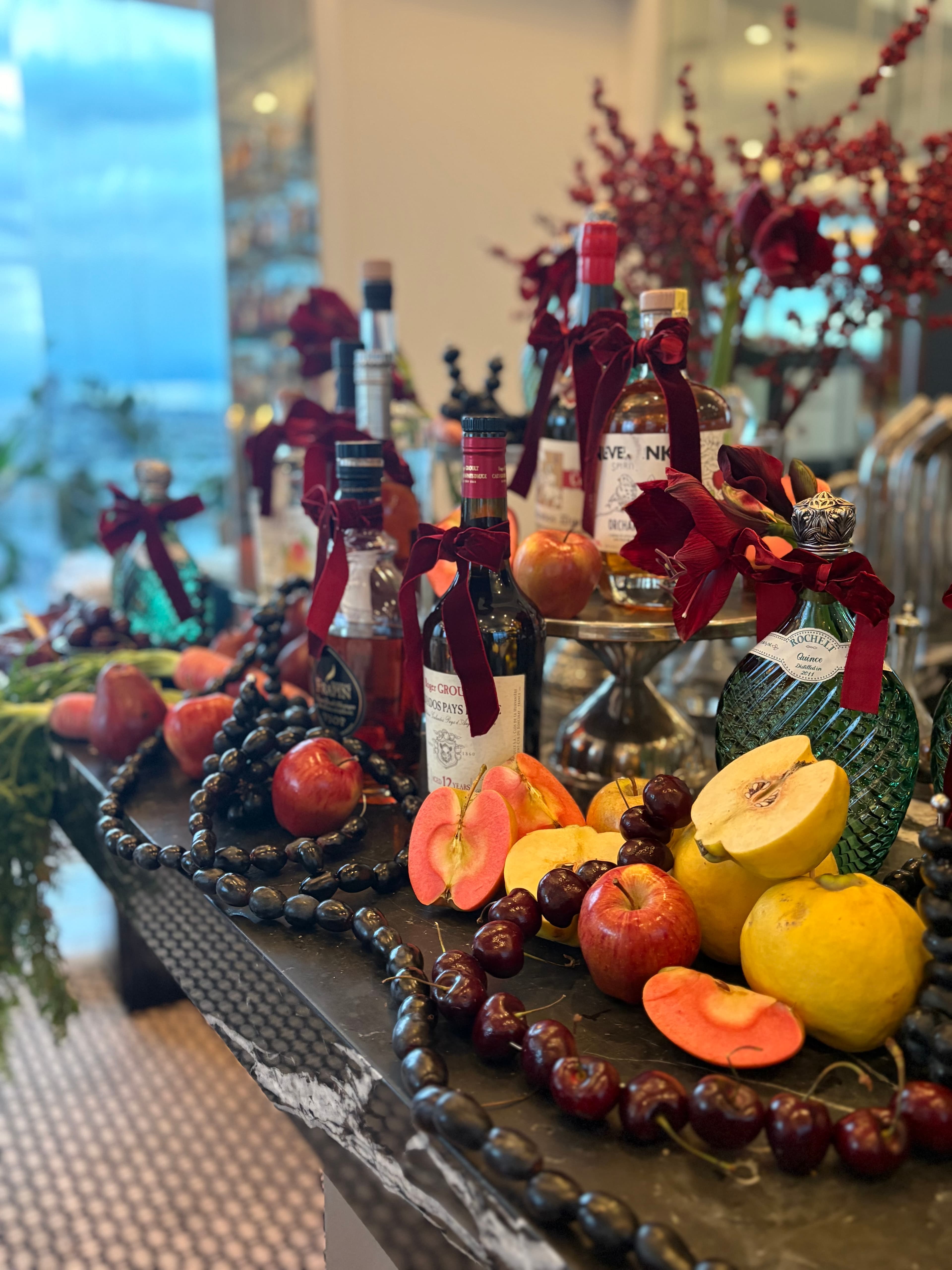 Bottles tied with burgundy bows among apples, grapes, and quince