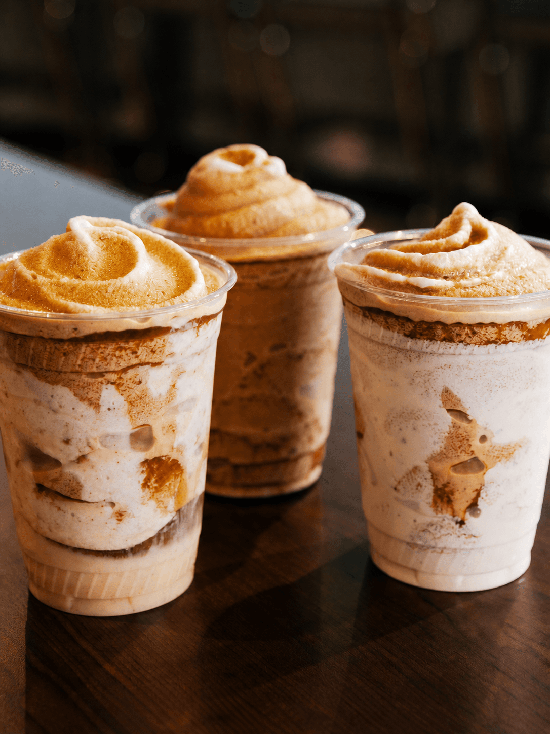Three layered frozen coffee drinks on a dark wooden table