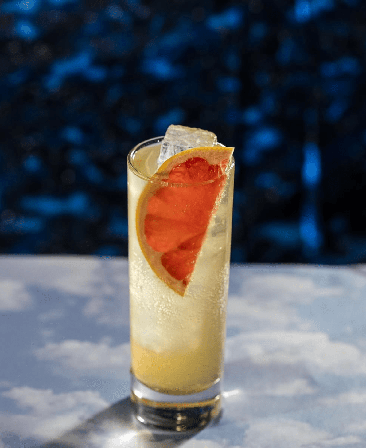 Grapefruit highball with a large clear ice cube against a deep blue background
