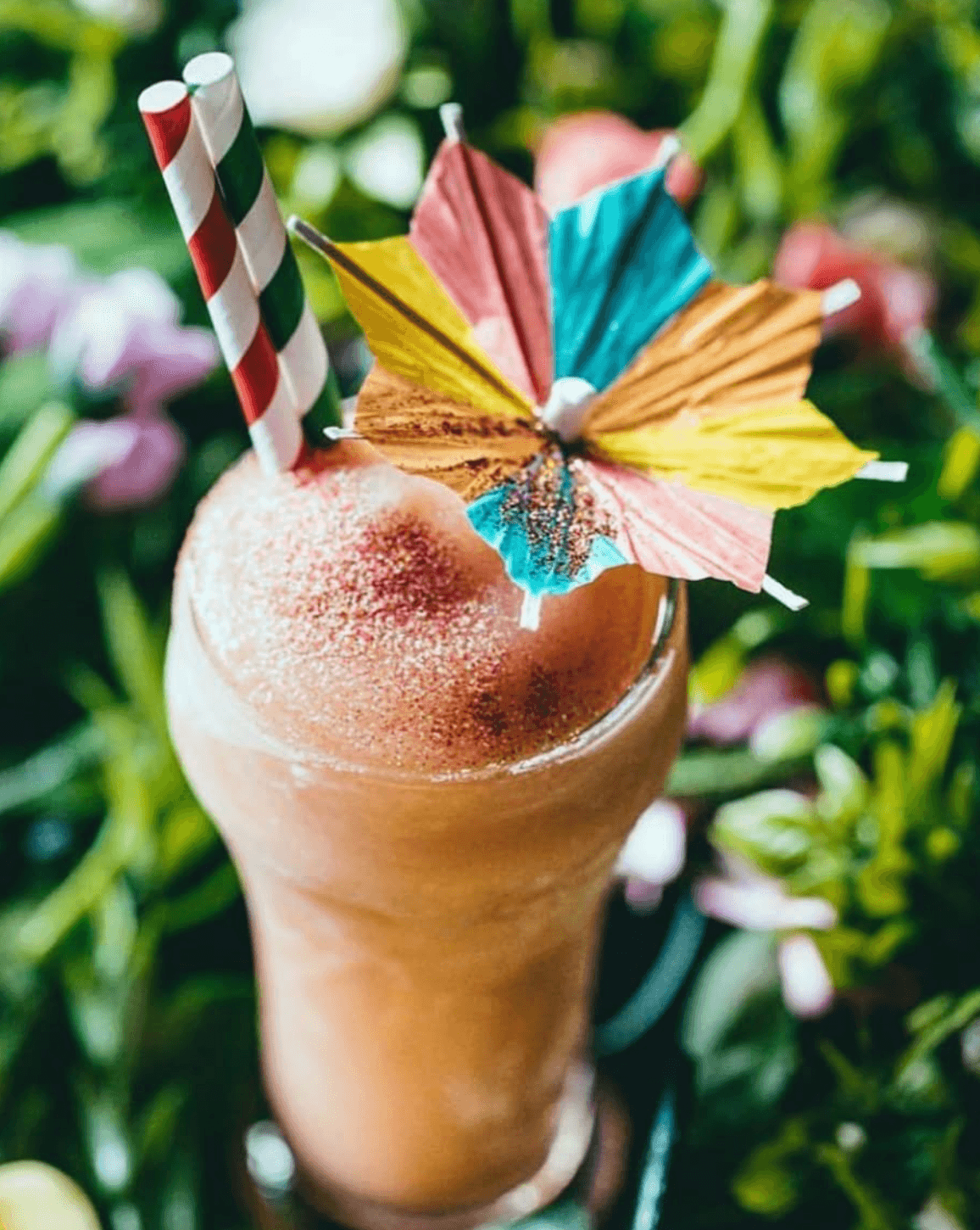 Frozen tropical drink with colorful paper umbrellas and striped straws among flowers