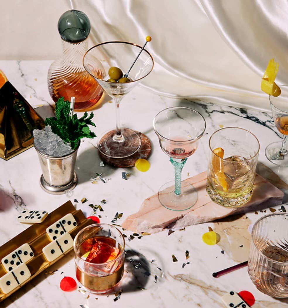 Cocktails, glassware, citrus, and dominoes arranged on a marble table