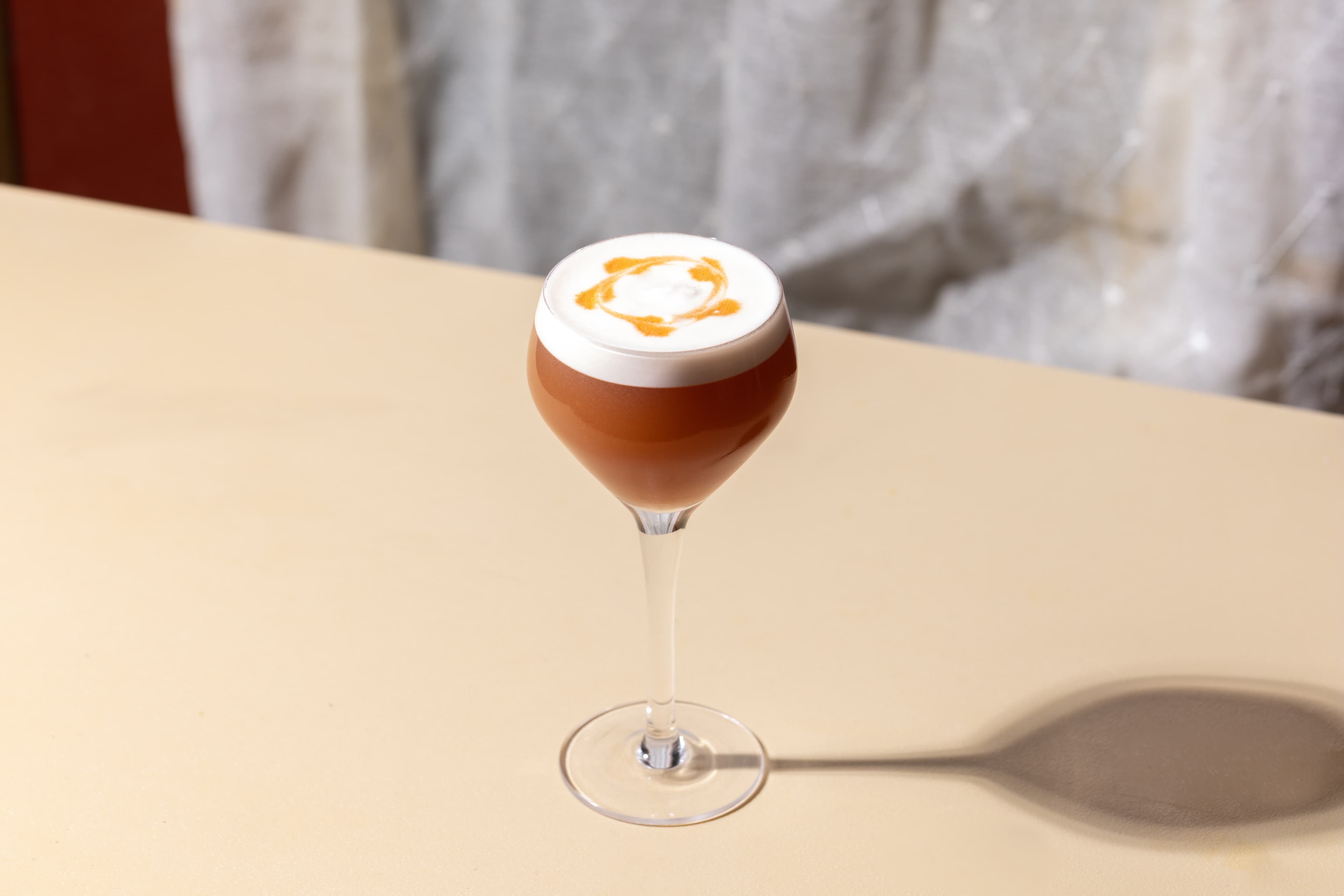 Foamy amber cocktail in a coupe casting a long shadow