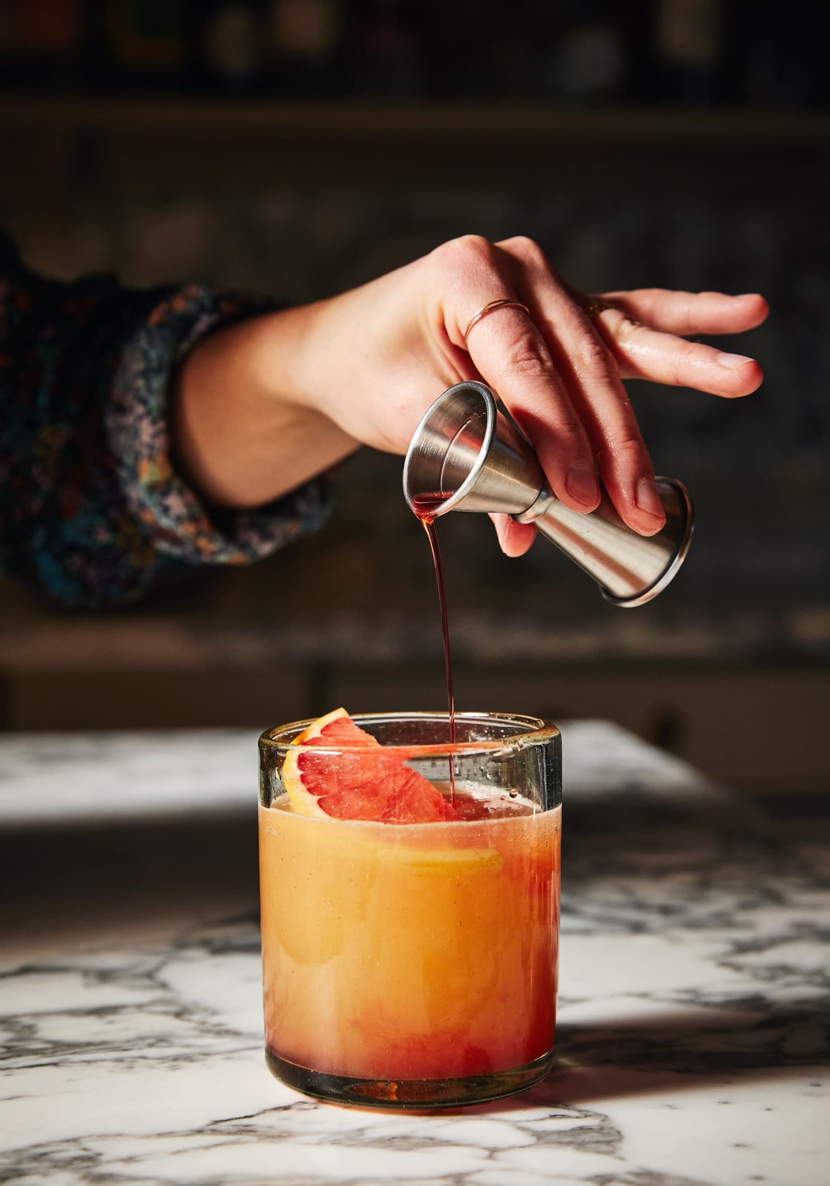 Hand pouring a dark ingredient into a grapefruit cocktail