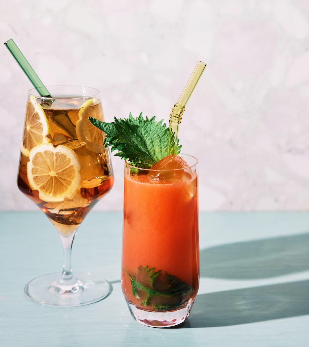 Two colorful citrus drinks with glass straws on a pale blue table