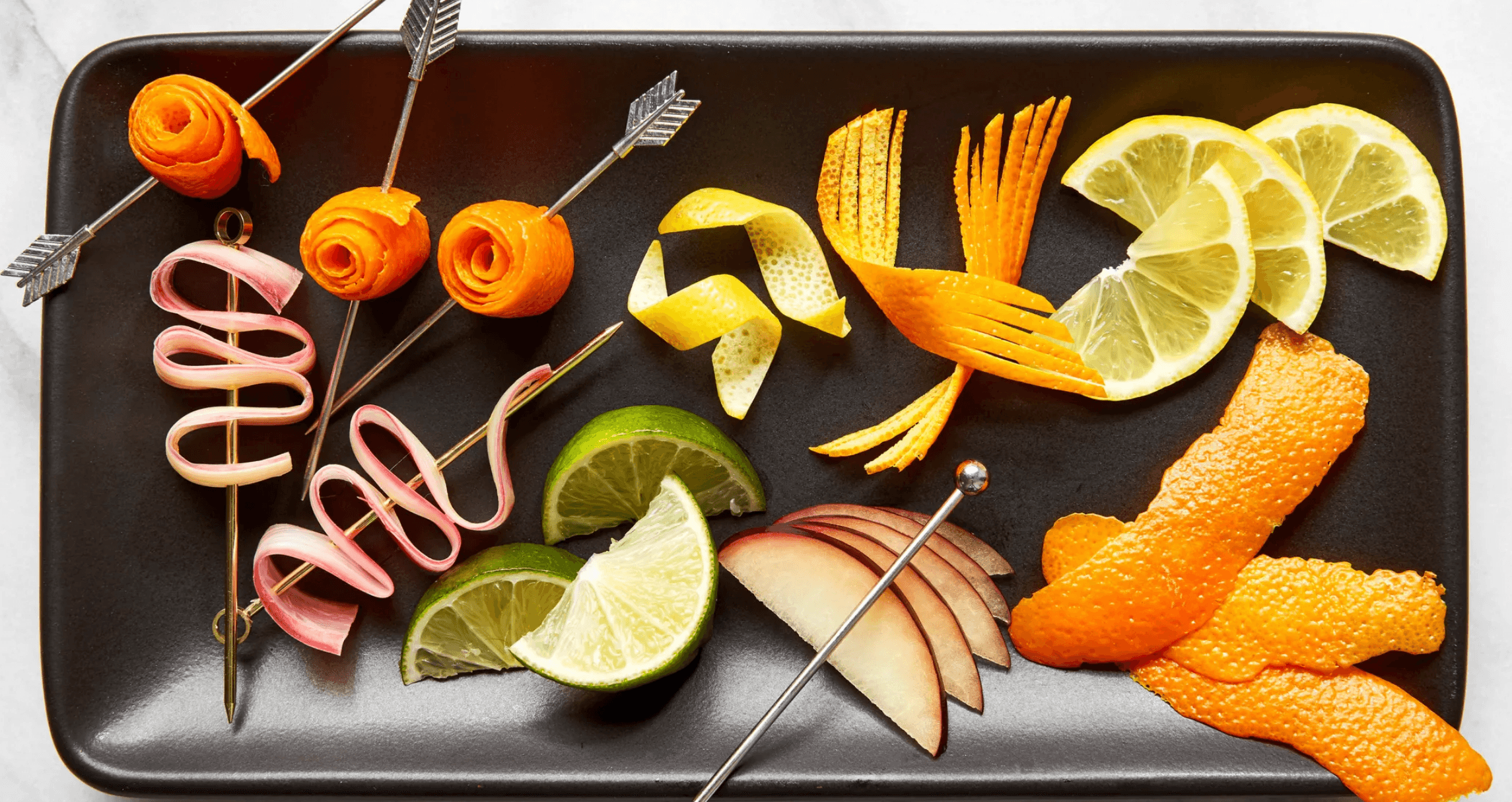 Creative citrus and rhubarb cocktail garnishes arranged on a black tray
